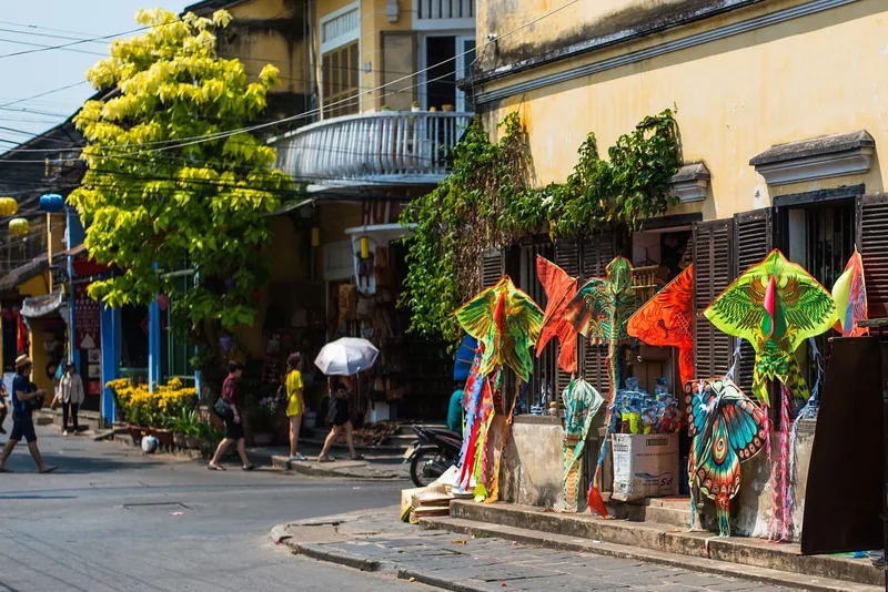 Colorful kites displayed outside a shophouse on a sunlit street in Hoi An's old town. Colorful kites displayed outside a shophouse on a sunlit street in Hoi An's old town.