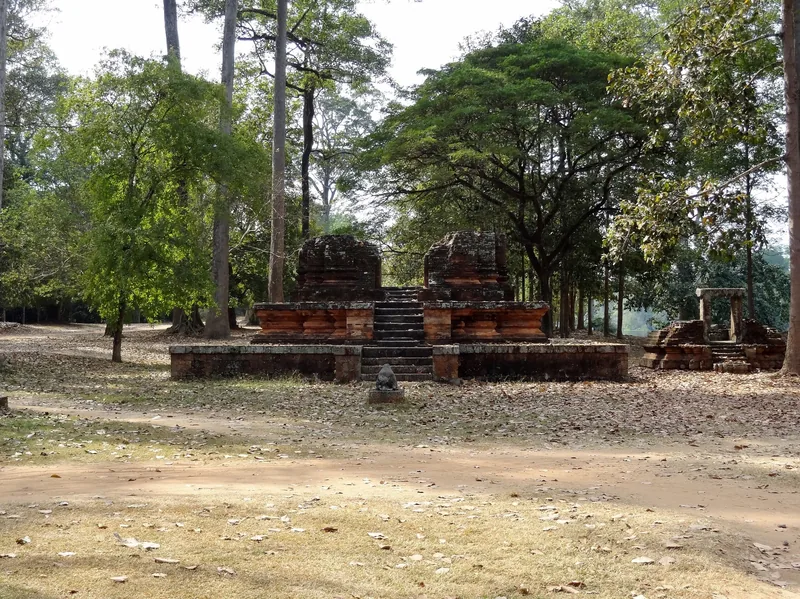 Weathered brick towers and stone steps of a small temple ruin surrounded by tall trees in Angkor Thom, Siem Reap.