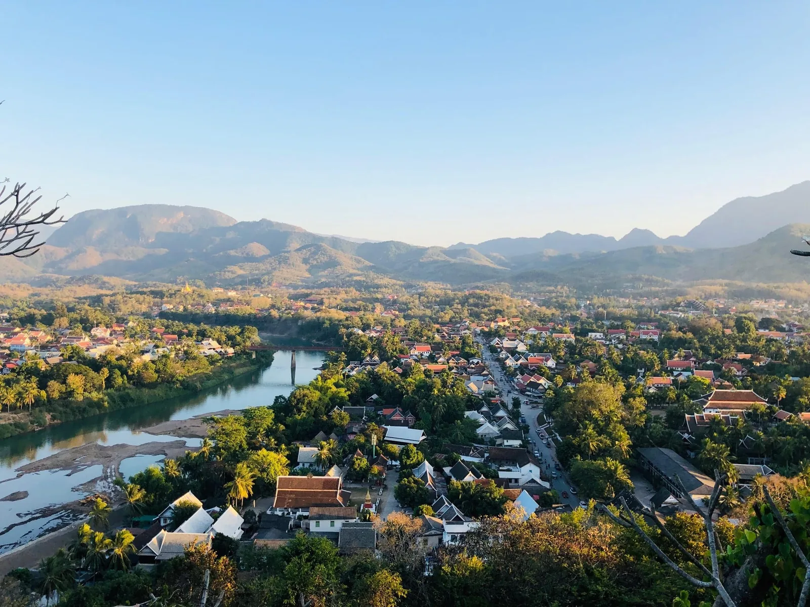 Aerial view over Luang Prabang's rooftops and river bend, framed by misty mountains at sunrise