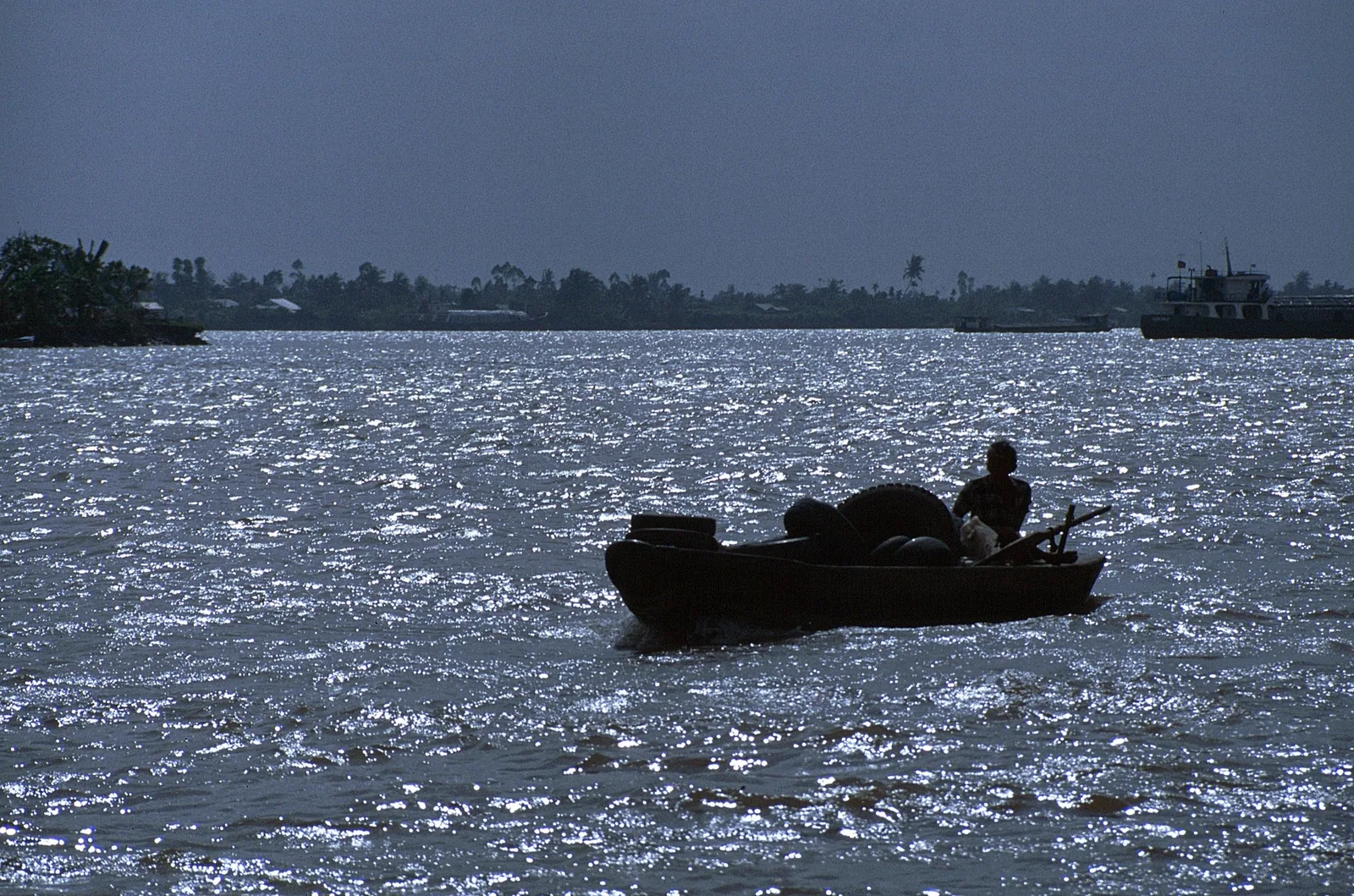 A boatman silhouetted against sparkling water steers a small wooden boat on the Mekong Delta river. A boatman silhouetted against sparkling water steers a small wooden boat on the Mekong Delta river.