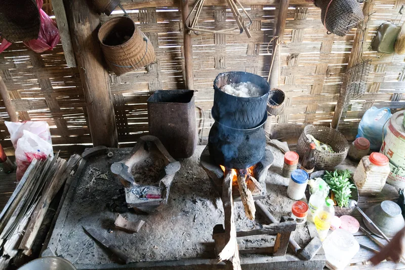 A traditional wood-fired kitchen with a soot-blackened pot cooking over open flame in Na Luang village near Nong Khiaw, Laos.
