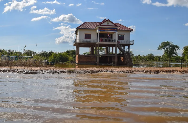 A stilted house with a red roof rises above the muddy waters near Kampong Phluk, Siem Reap.