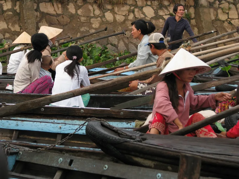 Boatwomen in conical hats sit among wooden rowboats waiting for passengers in the Mekong Delta.