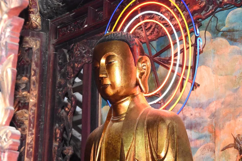 A gilded Buddha statue sits before colorful neon rings inside a temple in the Mekong Delta.