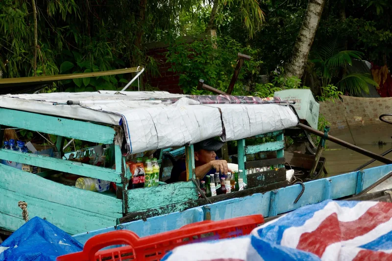 A vendor sits inside a turquoise wooden boat selling drinks and snacks on the Mekong Delta near Can Tho.