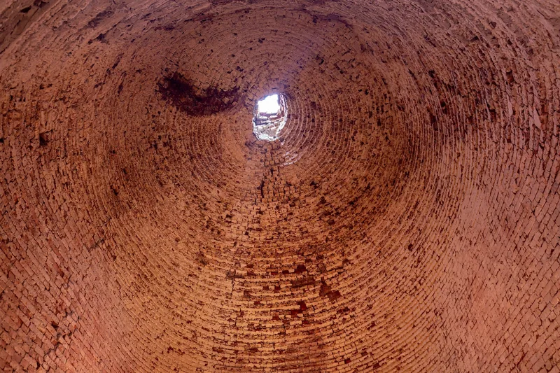 Looking up inside a tall brick kiln in the Mekong Delta, its curved walls spiraling toward a small opening of light.