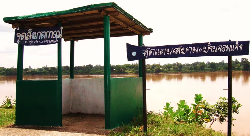 A green viewing pavilion with Thai signage overlooks the wide, muddy Mekong River near a border marker.